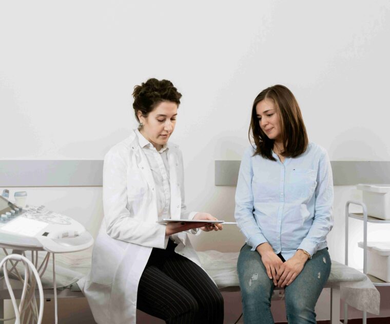 Woman sitting with doctor on bed with doctor showing information on tablet