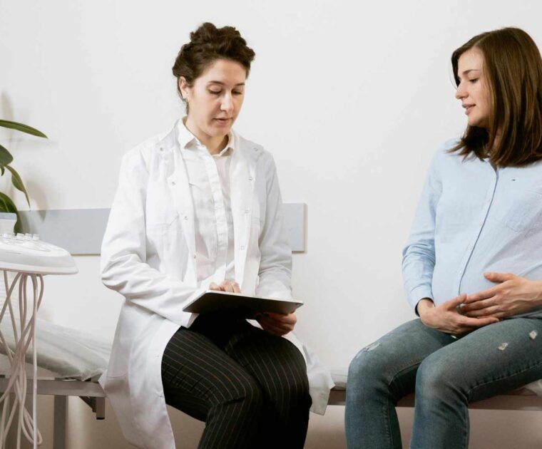 Pregnant woman sitting with doctor holding tablet device