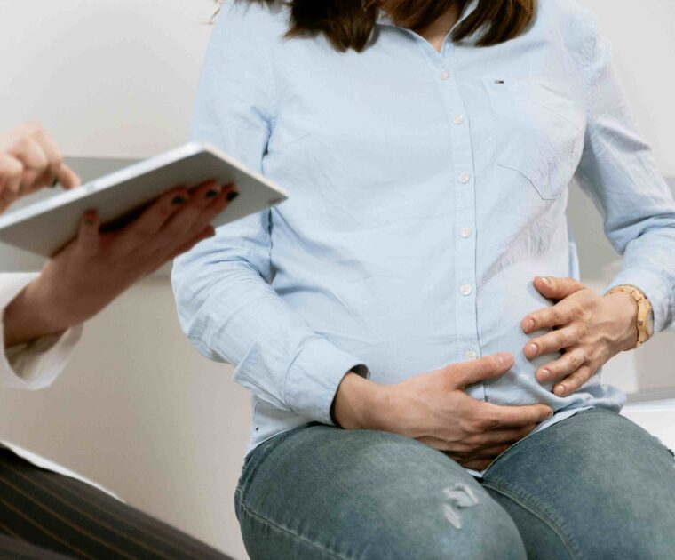 Pregnant woman holding stomach with doctor sitting next to woman holding tablet