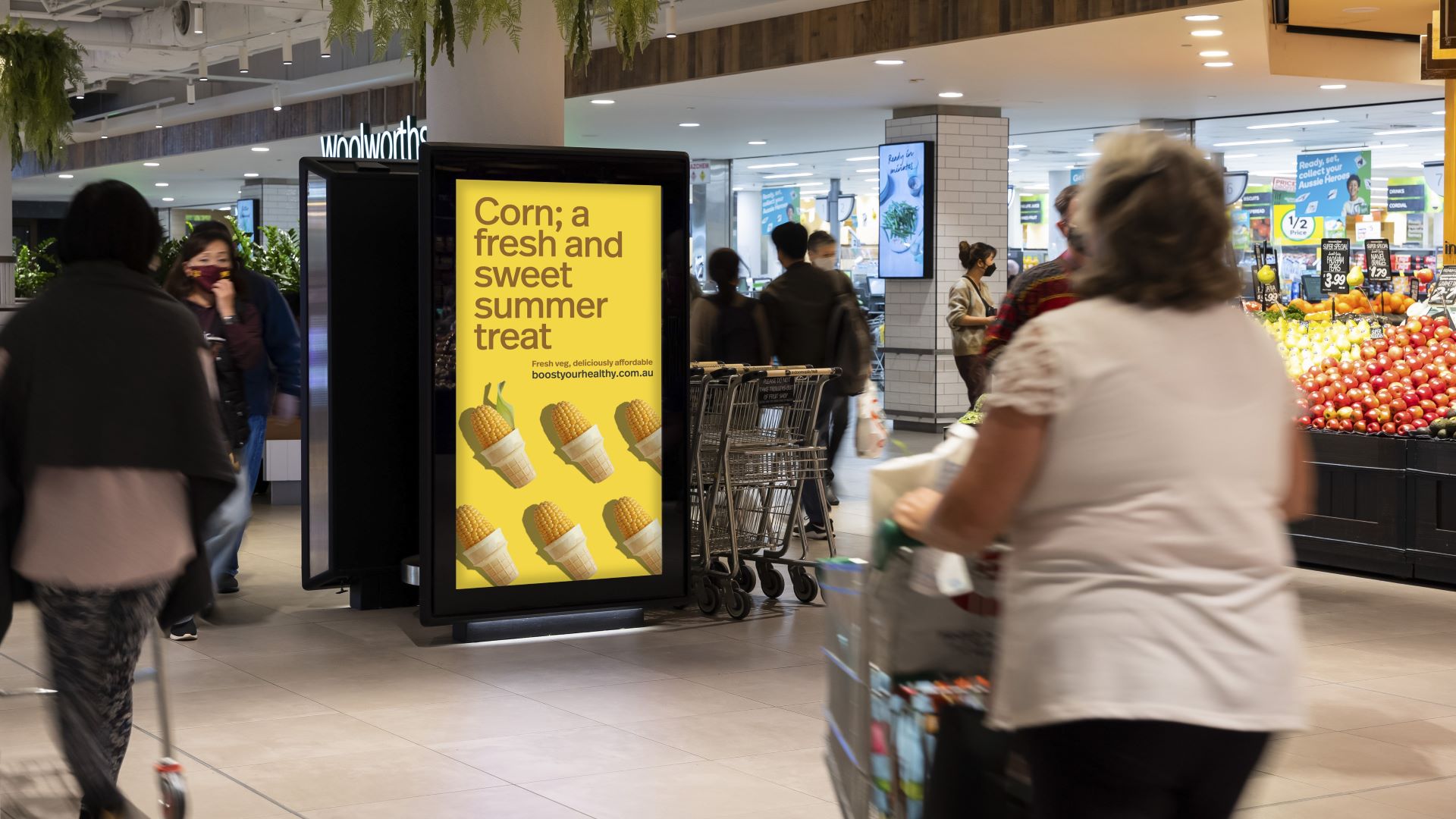 A bright advertising sign outside a supermarket reads, Corn, a fresh and sweet summer treat