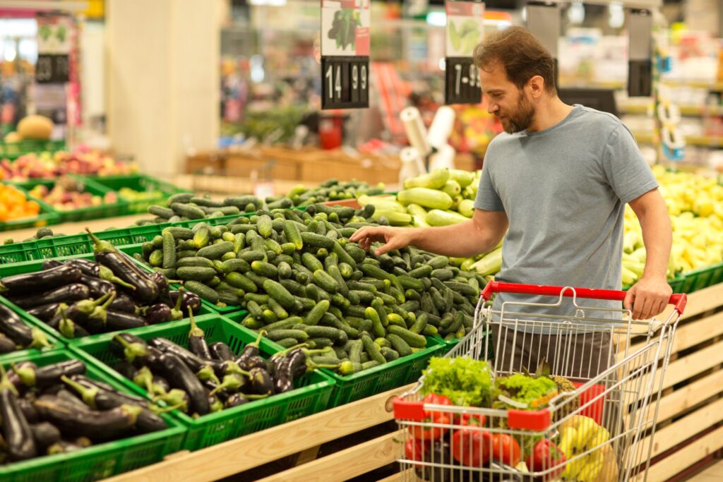 A man grocery shopping with a trolley in the fruit and vegetable aisle