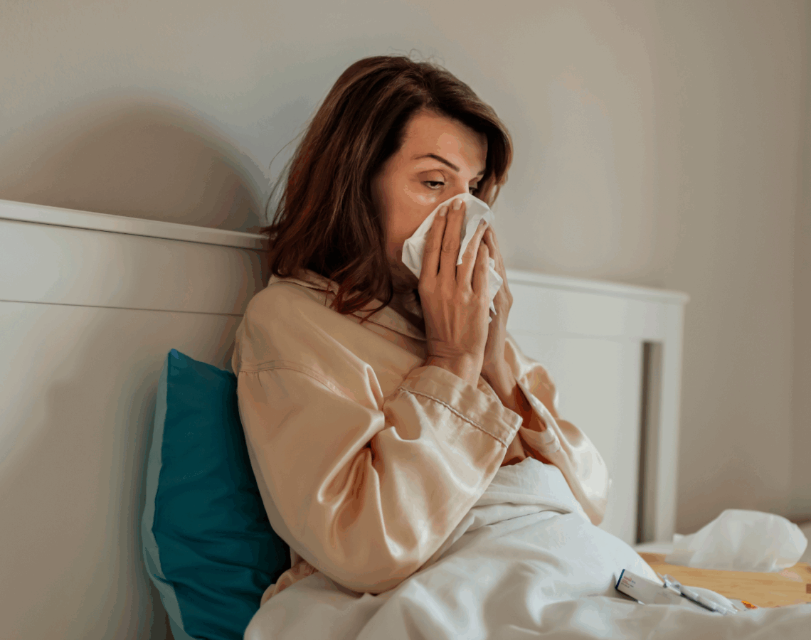 A person blowing their nose while sitting up in bed