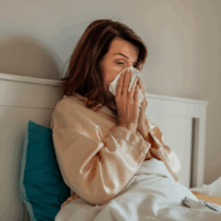 A person blowing their nose while sitting up in bed