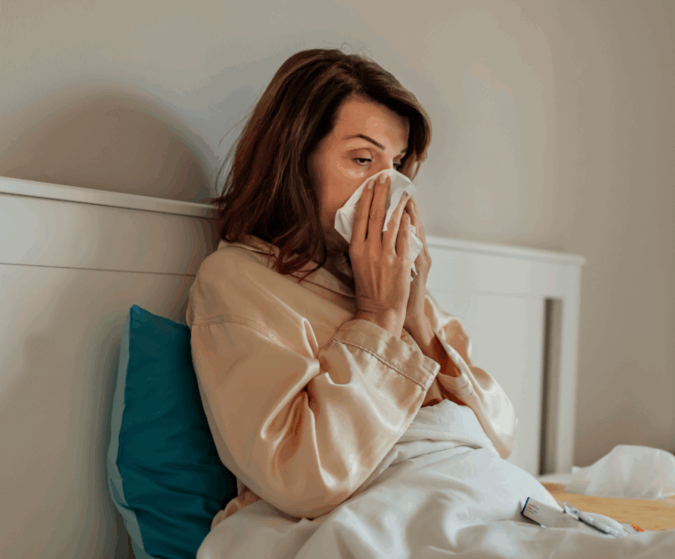 A person blowing their nose while sitting up in bed