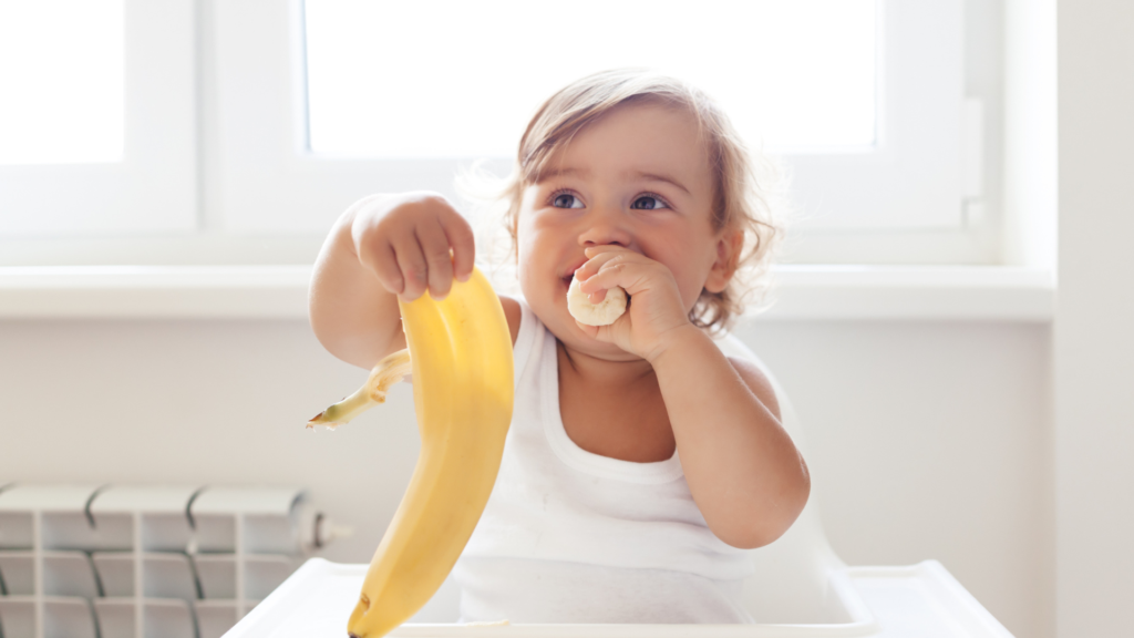 A young child in a high chair eating a banana