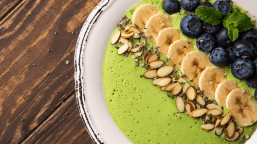 A close up shot of a green smoothie bowl with banana, berries and slivered almonds