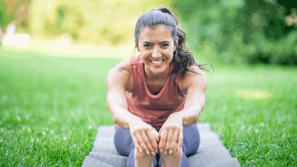 A woman stretching on a yoga mat outside practicing active recovery
