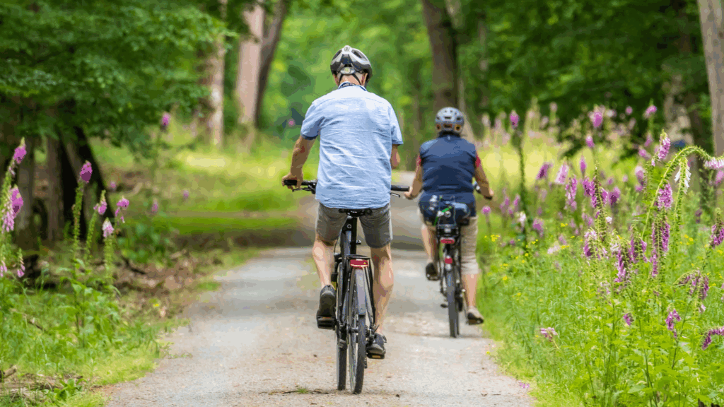 Two individuals bike riding on gravel road with bush land.