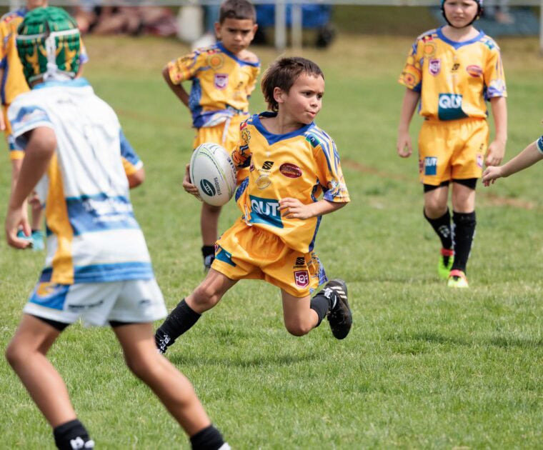 Young person holding NRL ball on a field.
