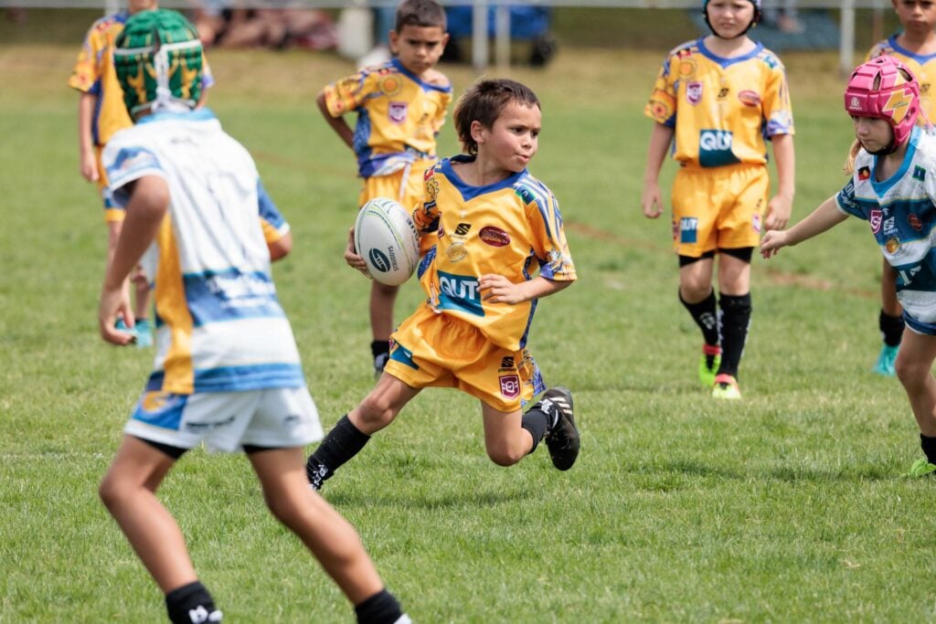Young person holding NRL ball on a field.
