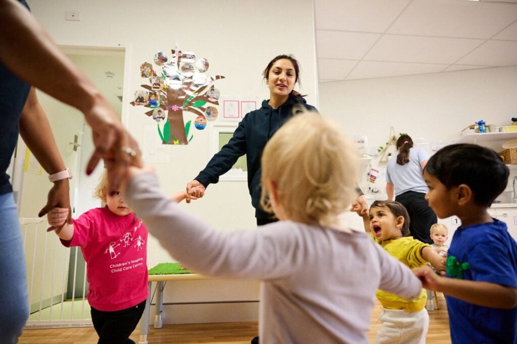 Children and educator holding hands in a circle, in a classroom.