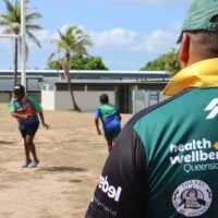Adult male rugby players watch on as children play rugby on the field