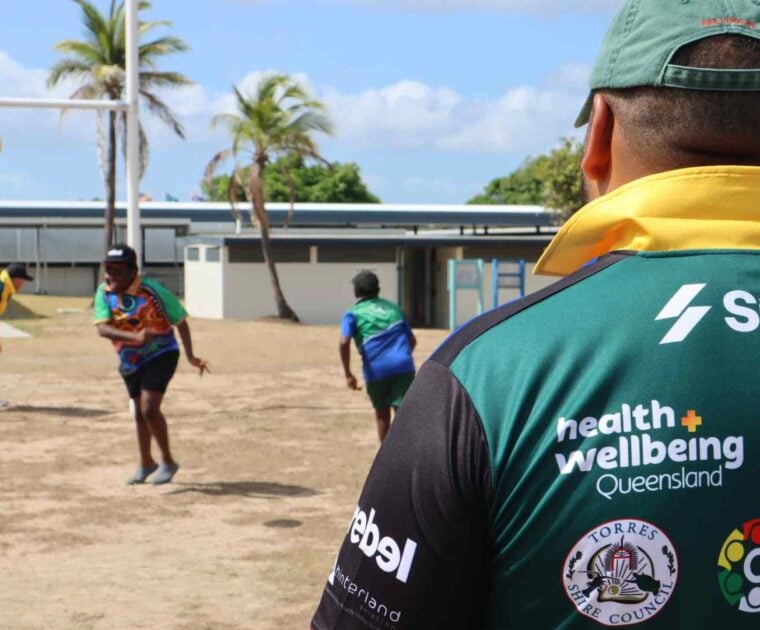 Adult male rugby players watch on as children play rugby on the field