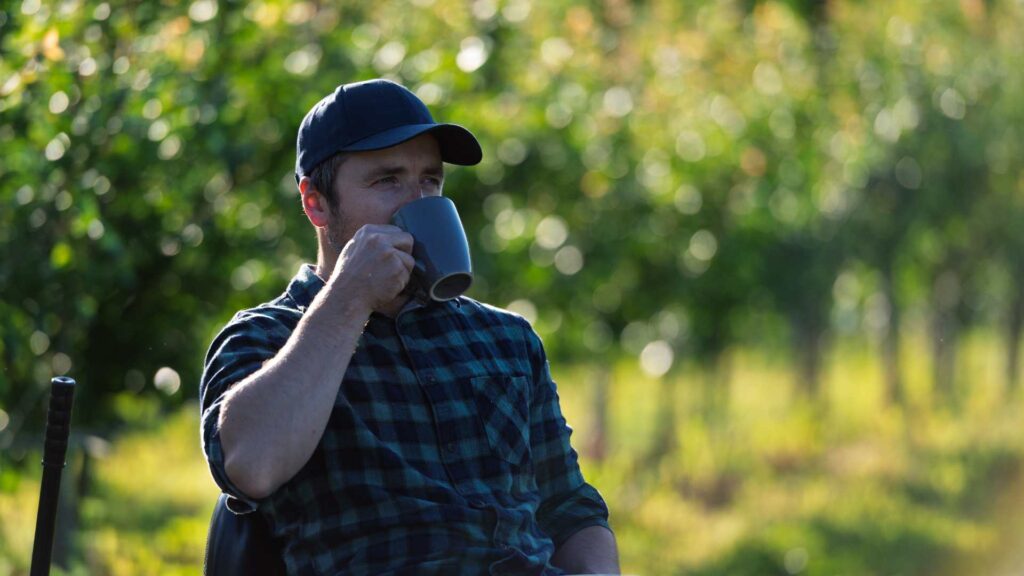Man sips from a mug while sitting outside amongst nature