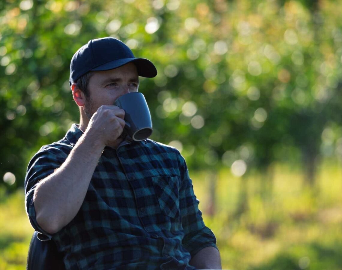 Man sips from a mug while sitting outside amongst nature