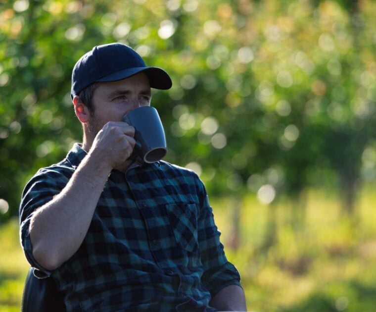 Man sips from a mug while sitting outside amongst nature