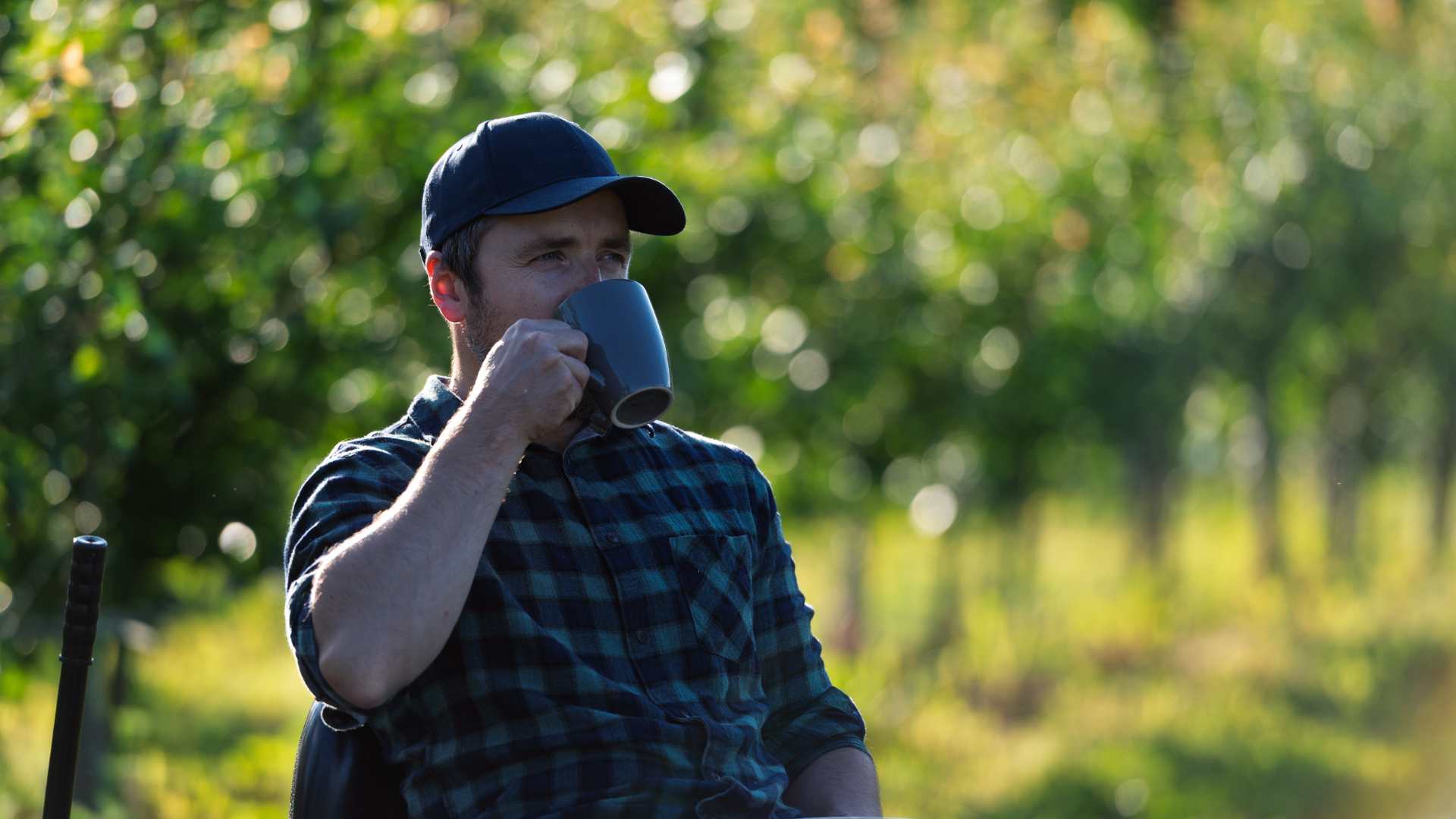Man sips from a mug while sitting outside amongst nature