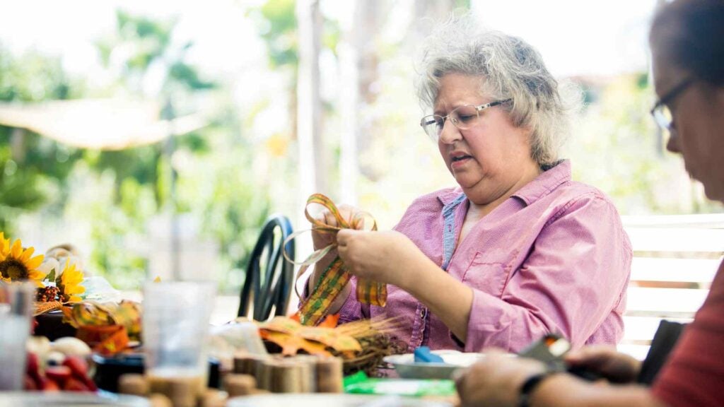 Older woman does crafts at a table with friends