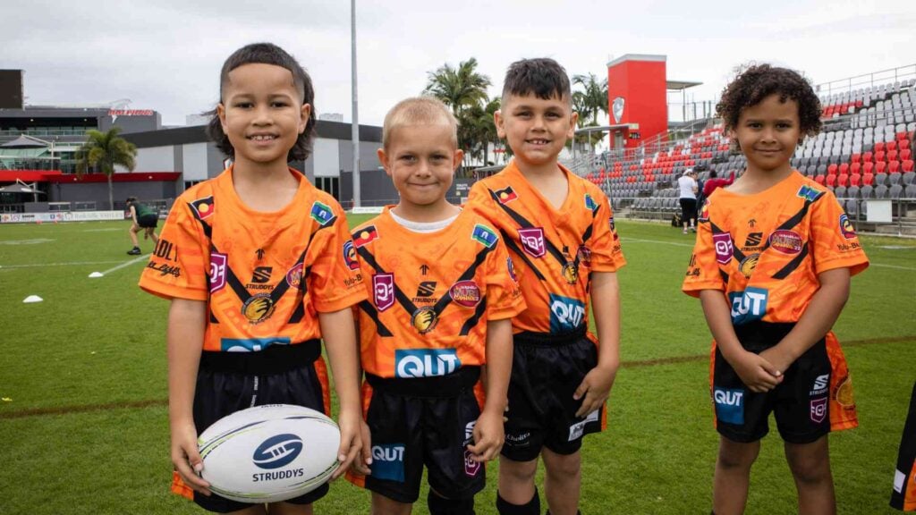 4 young boys pose on football field with one holding a football