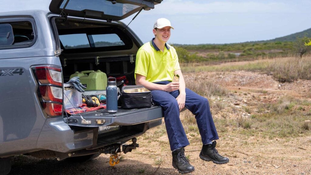Tradie sits on the back of his ute holding a salad wrap for lunch