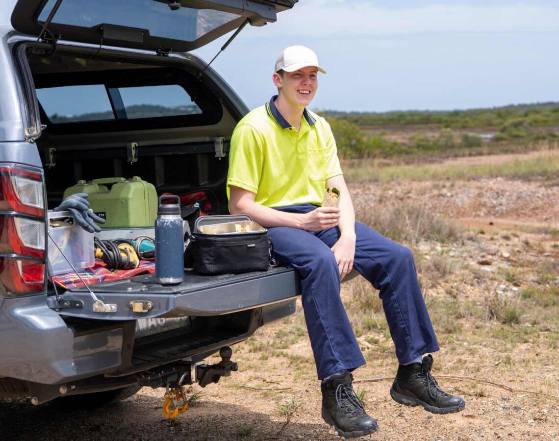 Tradie sits on the back of his ute holding a salad wrap for lunch