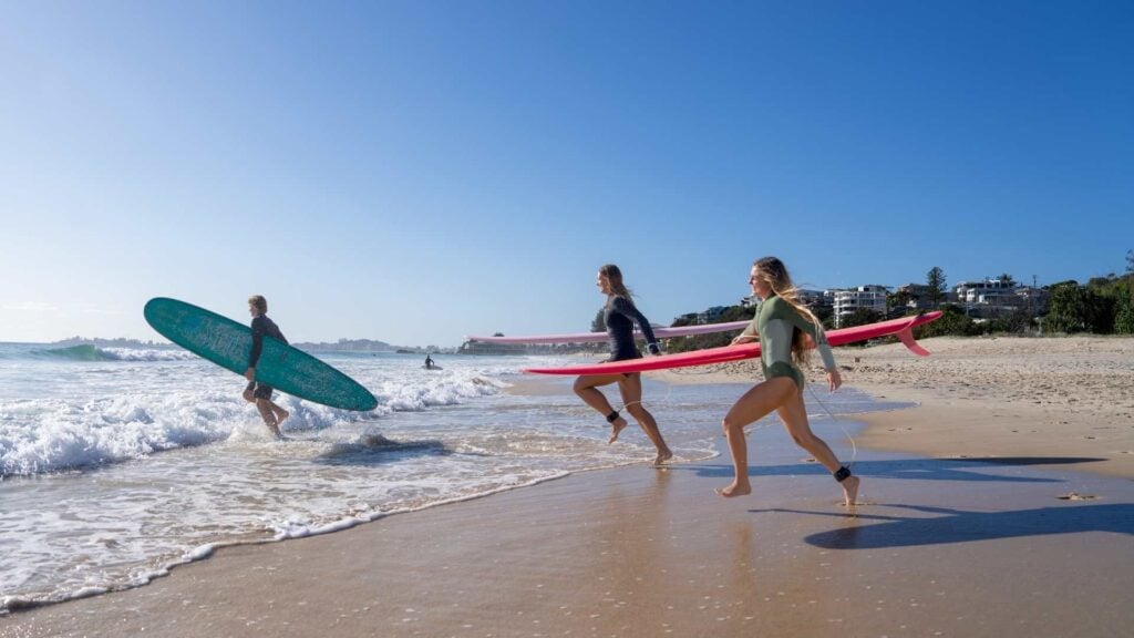 Three people run with surfboards into the ocean
