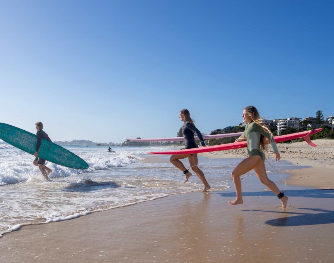 Three people run with surfboards into the ocean