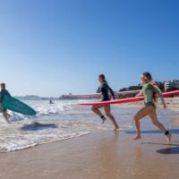 Three people run with surfboards into the ocean