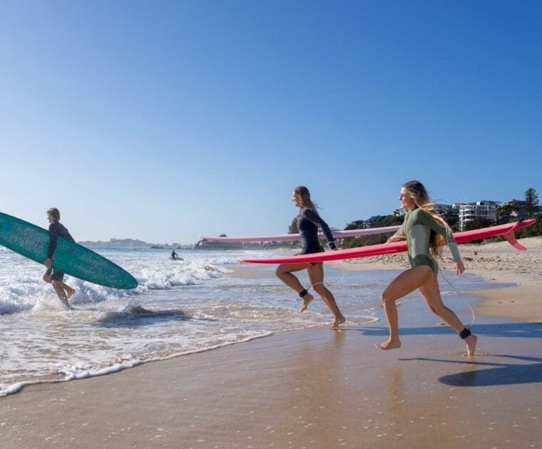 Three people run with surfboards into the ocean