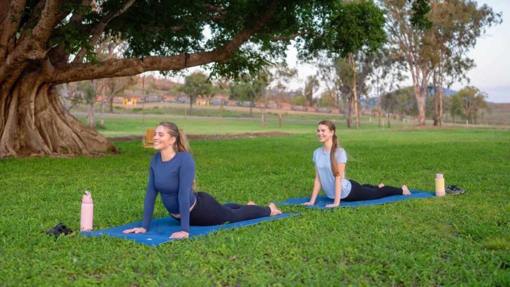 Two woman do yoga under a tree outside