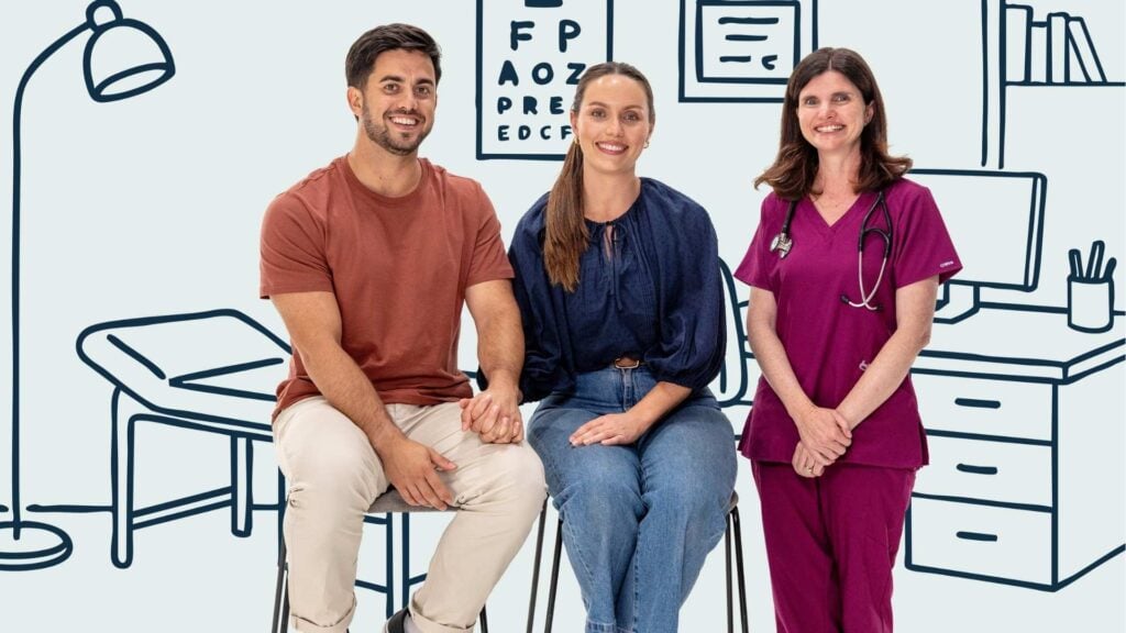 Young couple sit holding hands beside a doctor all smiling to camera