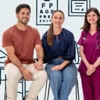 Young couple sit holding hands beside a doctor all smiling to camera