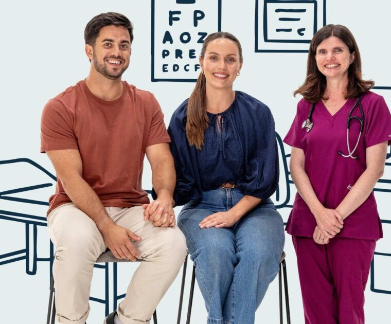 Young couple sit holding hands beside a doctor all smiling to camera