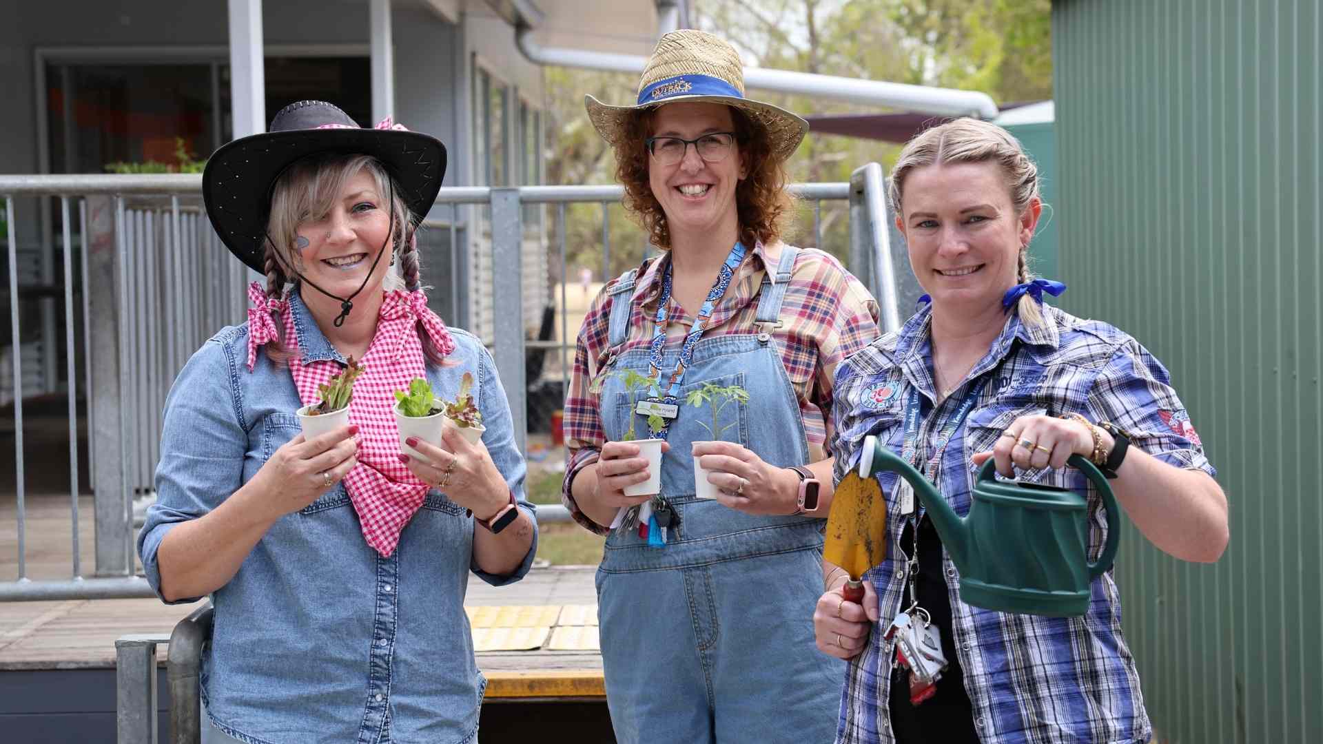 Teachers pose to camera dressed as farmers and holding plants and a watering can
