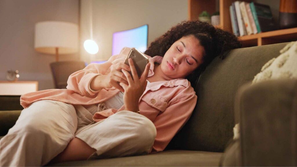 Woman sits on couch scrolling her phone