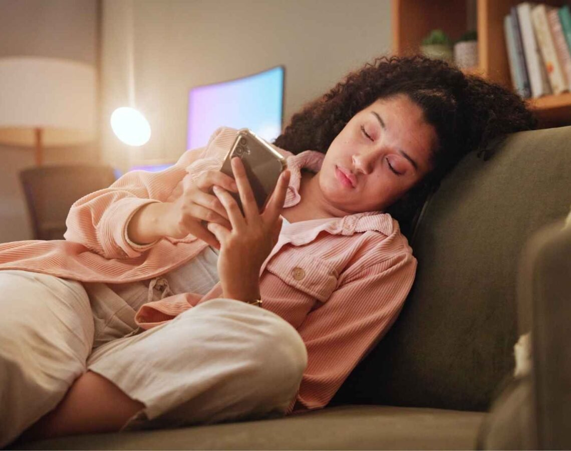 Woman sits on couch scrolling her phone