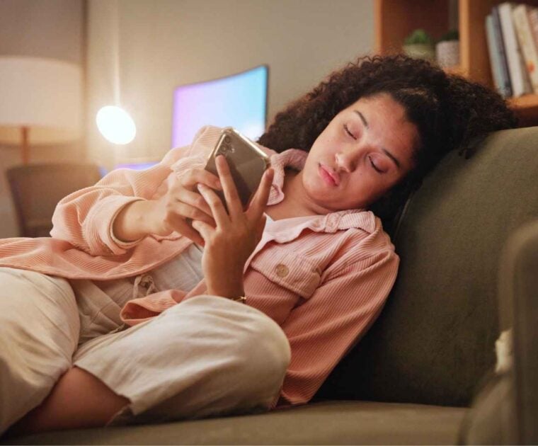 Woman sits on couch scrolling her phone