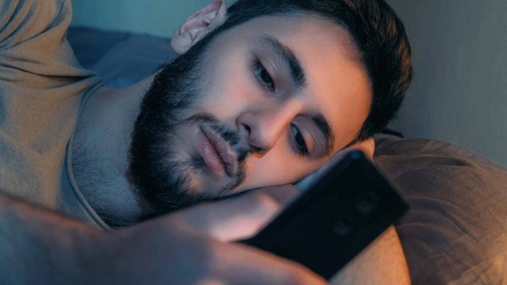 Man looks at phone in bed
