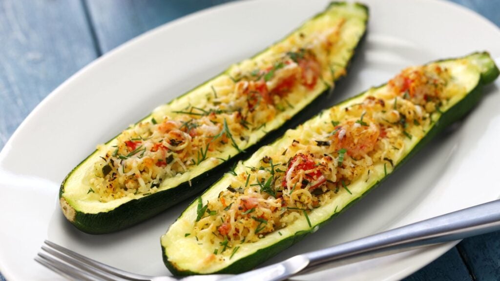 Two stuffed zucchini slices topped with vegetables, cheese and fresh herbs