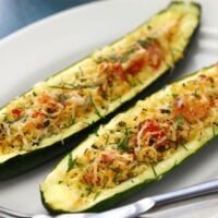 Two stuffed zucchini slices topped with vegetables, cheese and fresh herbs