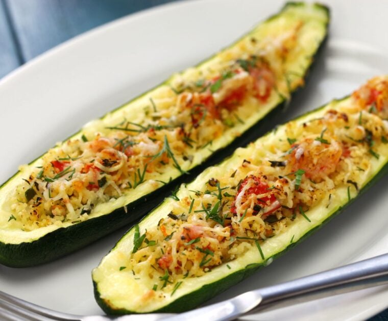 Two stuffed zucchini slices topped with vegetables, cheese and fresh herbs