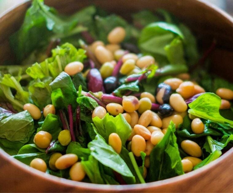 Wooden bowl filled with a mix of beans and leafy green salad