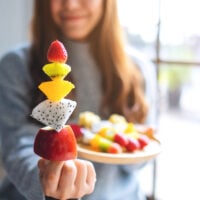 Closeup image of a woman holding and showing a fresh mixed fruits on skewers