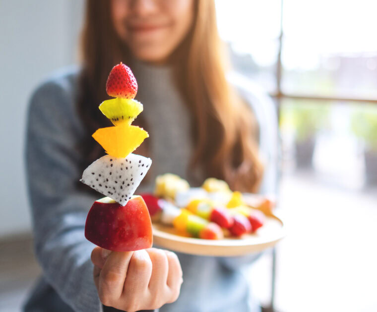 Closeup image of a woman holding and showing a fresh mixed fruits on skewers