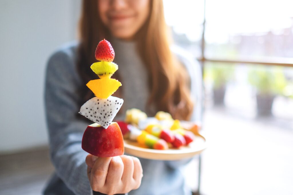 Closeup image of a woman holding and showing a fresh mixed fruits on skewers