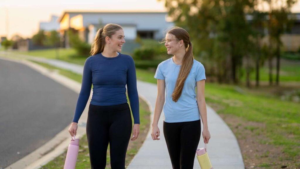 Two young woman walk together on a foot path wearing activewear