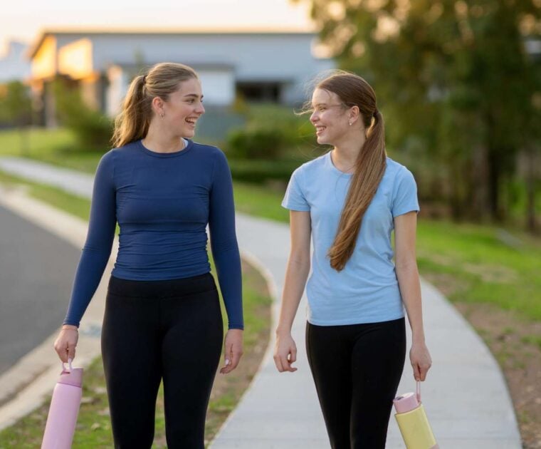 Two young woman walk together on a foot path wearing activewear