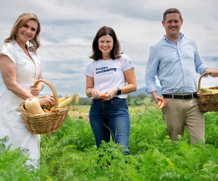 3 people stand in a crop field holding vegetables