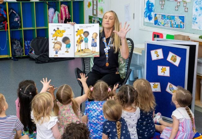 A woman reads a story to kindergarten children sitting on a group time mat
