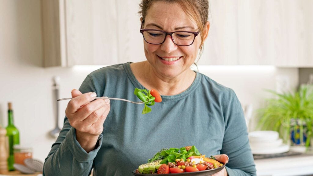 Woman eating healthy vegetable and legume salad in the kitchen